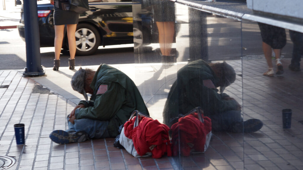 Homeless veteran sitting on sidewalk with duffel bag. Discover the links between substance abuse and veteran homelessness and how Foundation For Pops helps veterans reacclimate to civilian life.